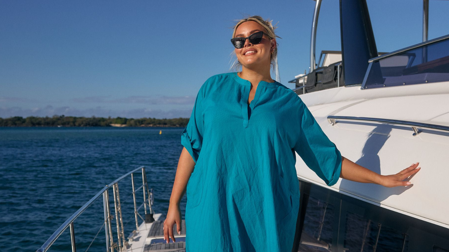 Woman with blonde hair poses on a boat wearing a teal cotton beach cover up
