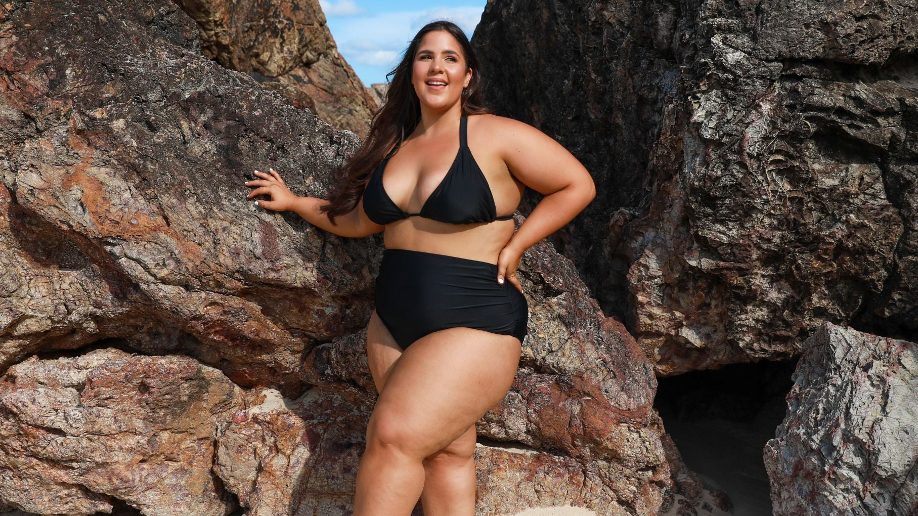 Woman with long brown hair wears black triangle bikini top and high waisted full coverage black bikini bottoms