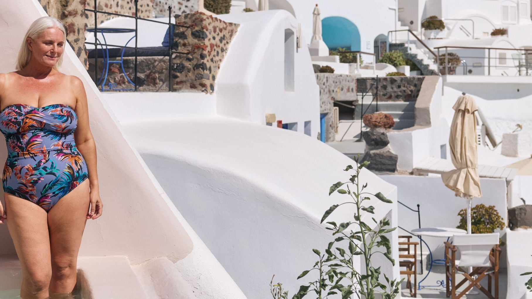 Woman poses on a terrace in Santorini wearing a tropical print strapless one piece swimsuit