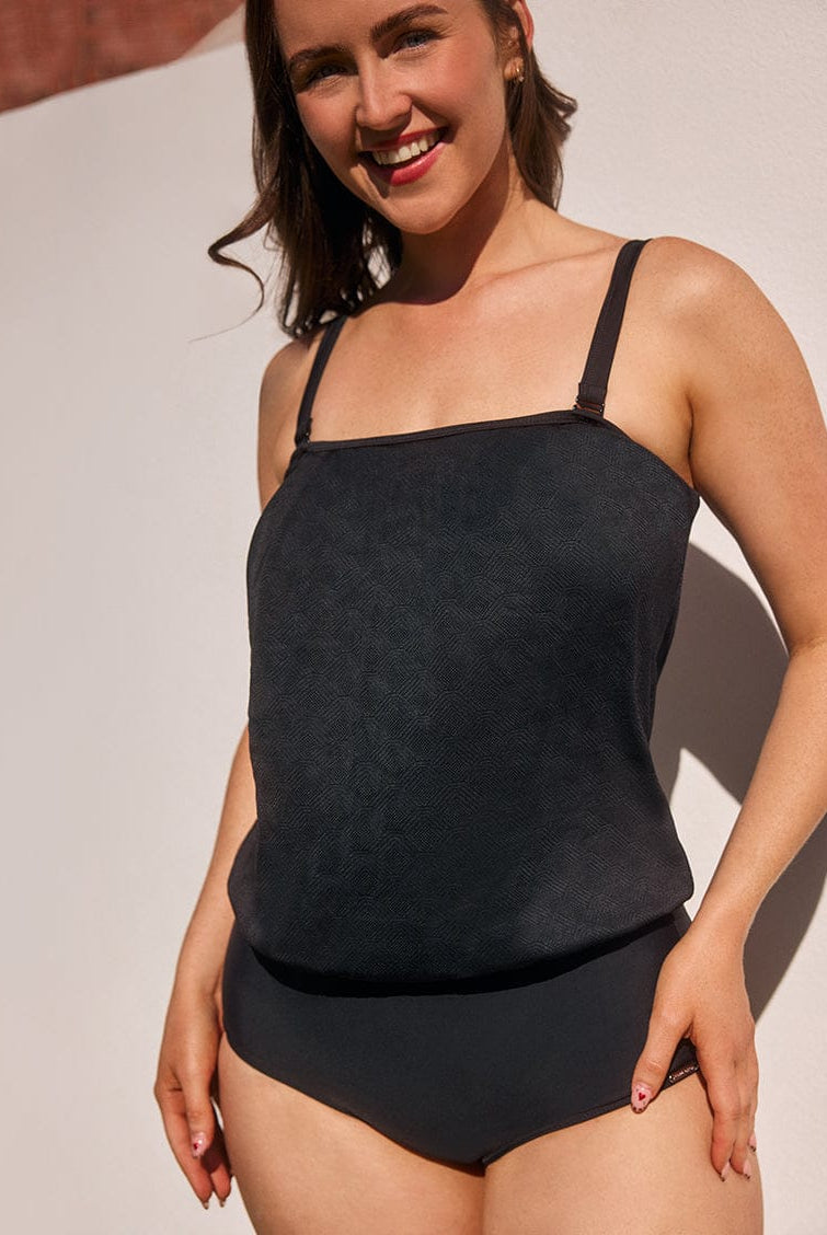 Woman wearing a black swimsuit against a neutral background