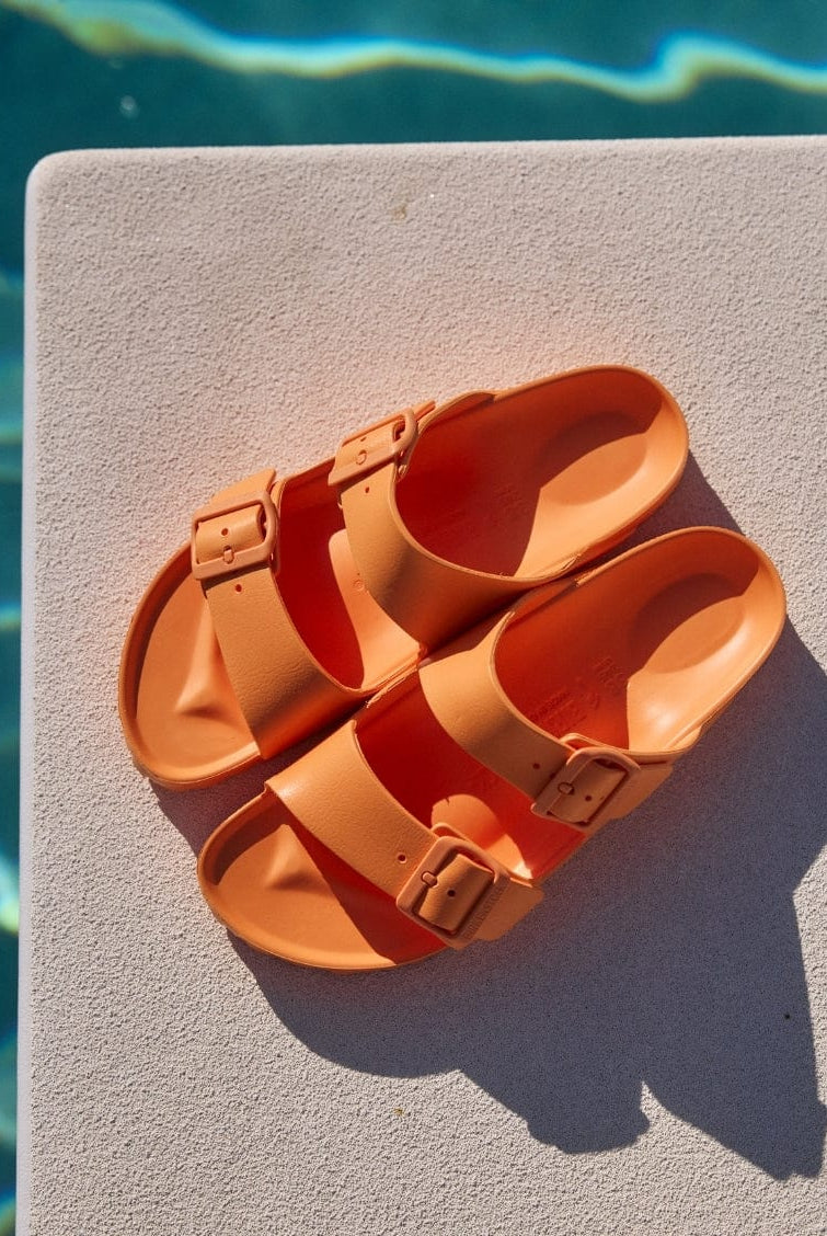 Pair of orange sandals on a diving board with water in the background