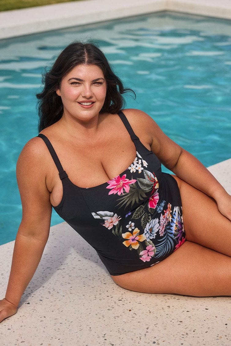 Brunette model wears black floral pool proof scoop beck one piece by the pool