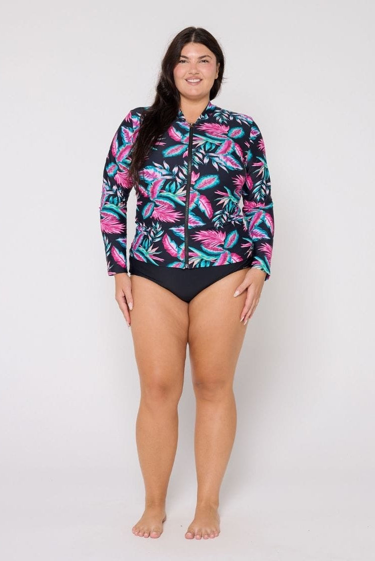 Woman wearing a colorful floral rash guard and black swimsuit bottom on a white background