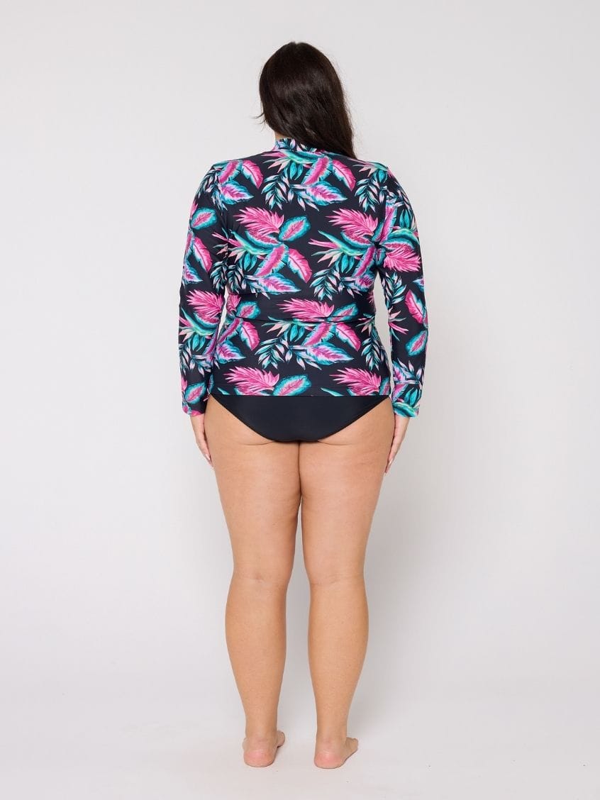 Person wearing a colorful tropical print long-sleeve shirt over a black swimsuit on a white background