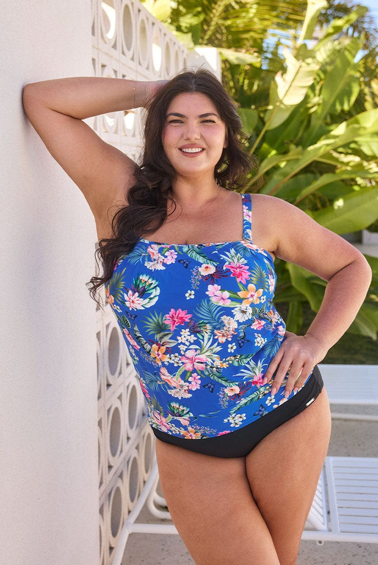 Brunette model wears flattering blue floral flouncy bandeau tankini top with straps that can be removed
