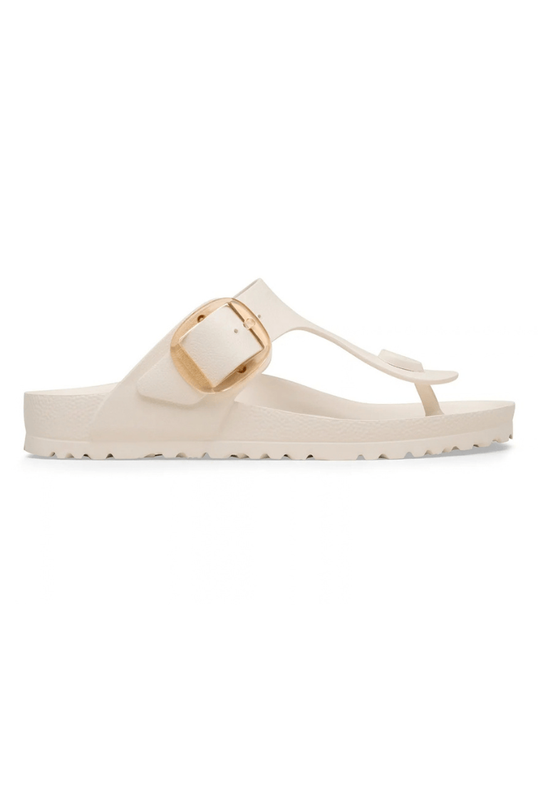A single cream-colored slide sandal with a wide strap, a gold-tone buckle, and a low wedge heel, shown in profile against a plain white background.