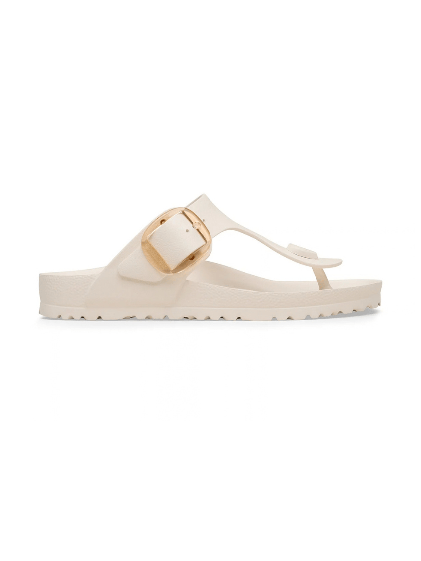 A single cream-colored slide sandal with a wide strap, a gold-tone buckle, and a low wedge heel, shown in profile against a plain white background.