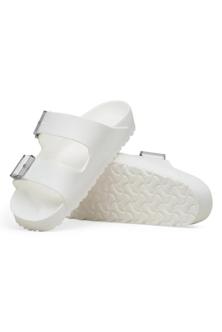 A pair of white double-strap slide sandals with textured soles and small silver buckle details, shown on a clean white background.
