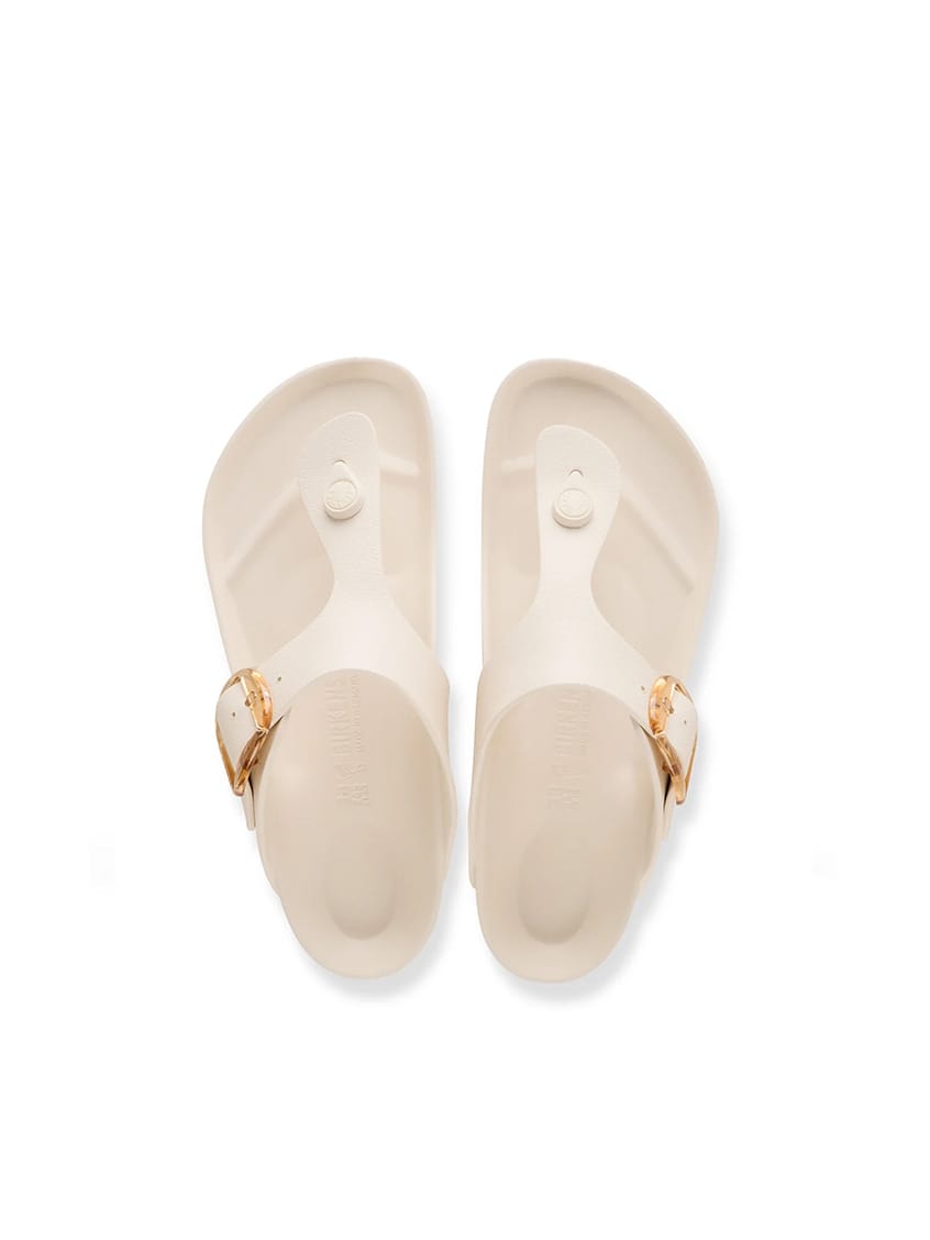 A pair of Birkenstock Thalia slide sandals in cream-colored foam with gold-tone buckle details, shown from a top-down view on a white background.