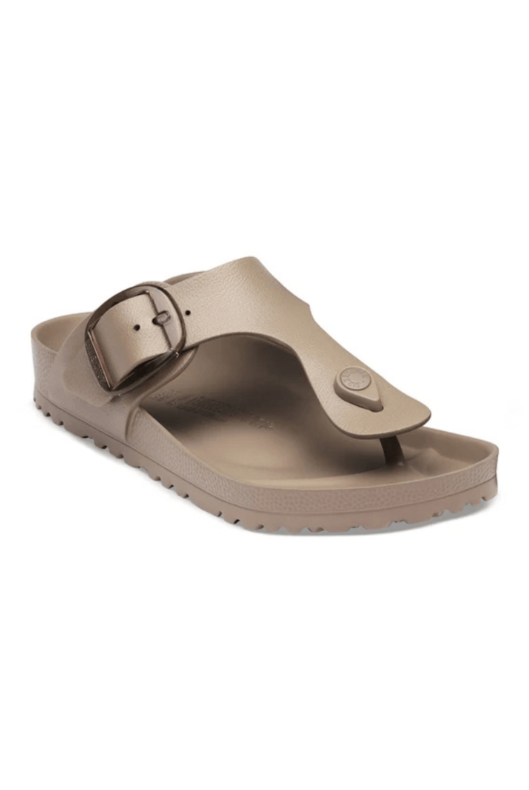 A single taupe-colored thong sandal with a wide strap featuring a large decorative buckle and a small circular button detail, shown against a plain white background.