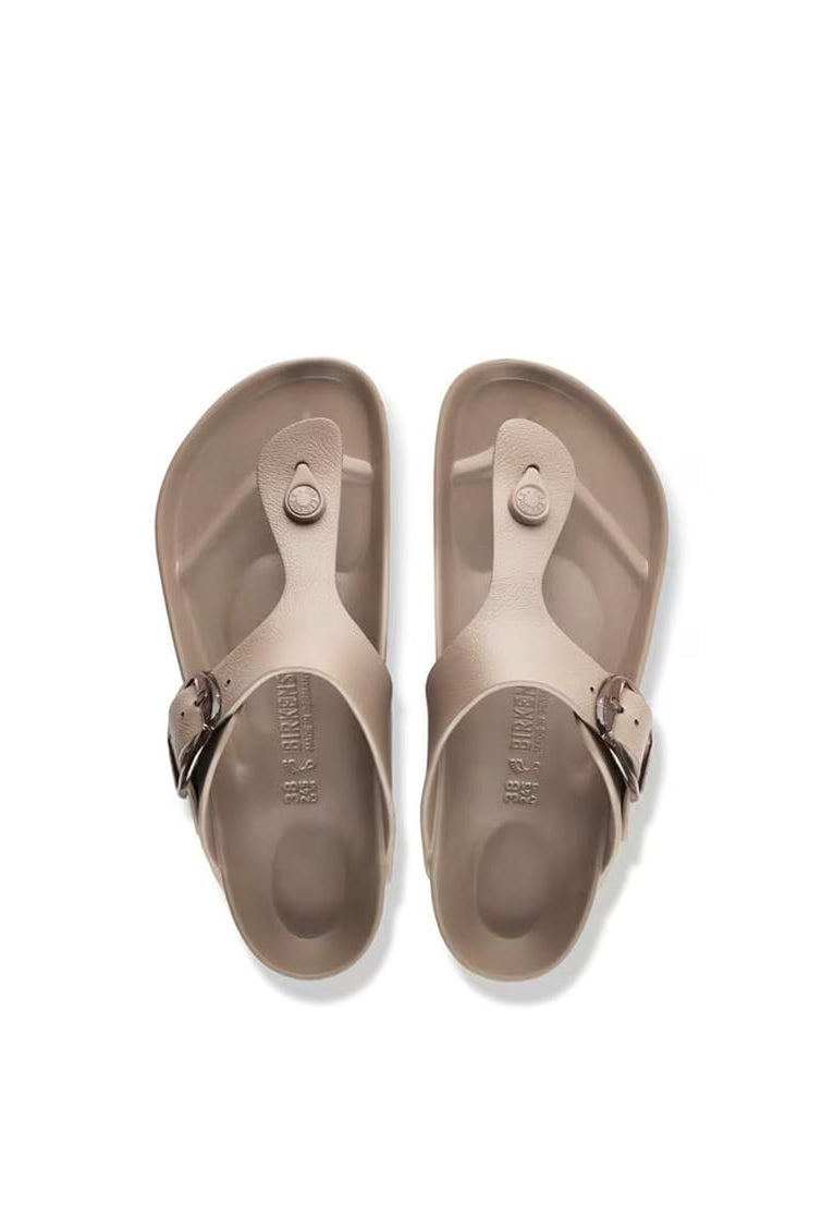 A pair of light taupe/beige thong sandals with dark metal buckles, shown from a top-down view on a white background.