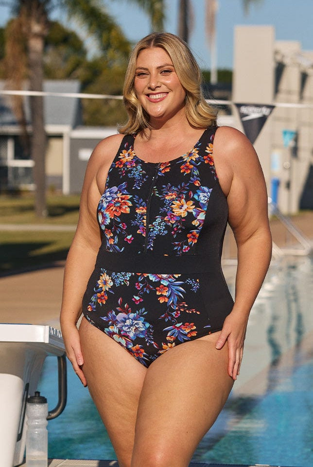 Model wearing black floral zip up swimsuit at pool