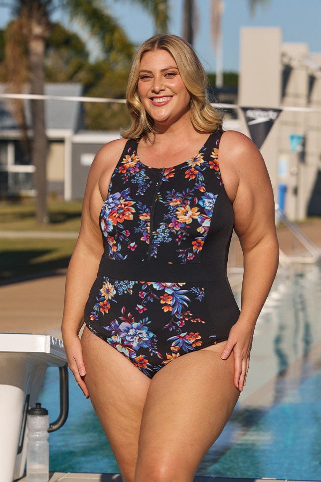 Model wearing black floral zip up swimsuit at pool