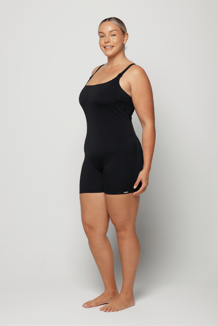 Woman wearing a black boyleg one piece against a white background