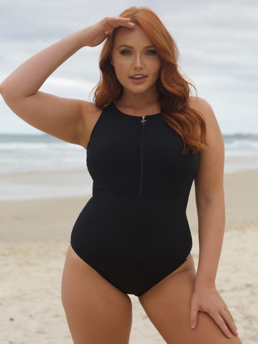 Woman in a black swimsuit standing on a beach with ocean in the background