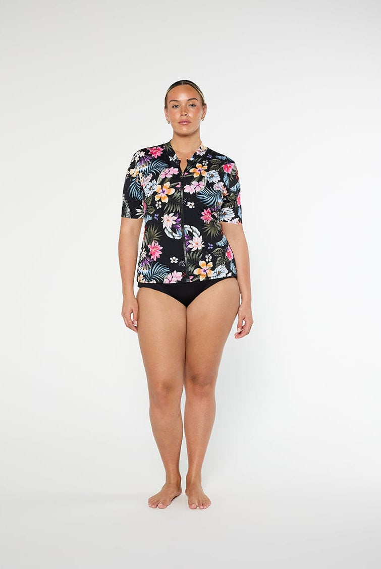 Woman wearing a floral short-sleeve shirt and black swimsuit bottom on a white background