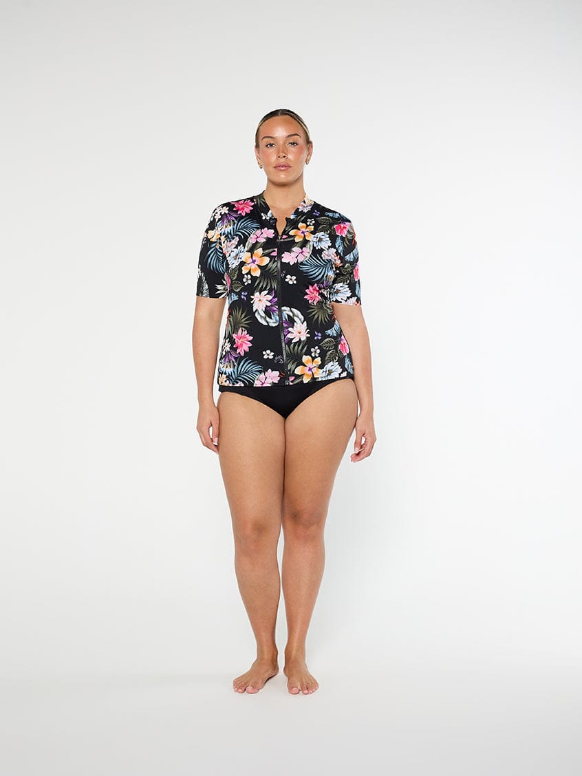 Woman wearing a floral short-sleeve shirt and black swimsuit bottom on a white background