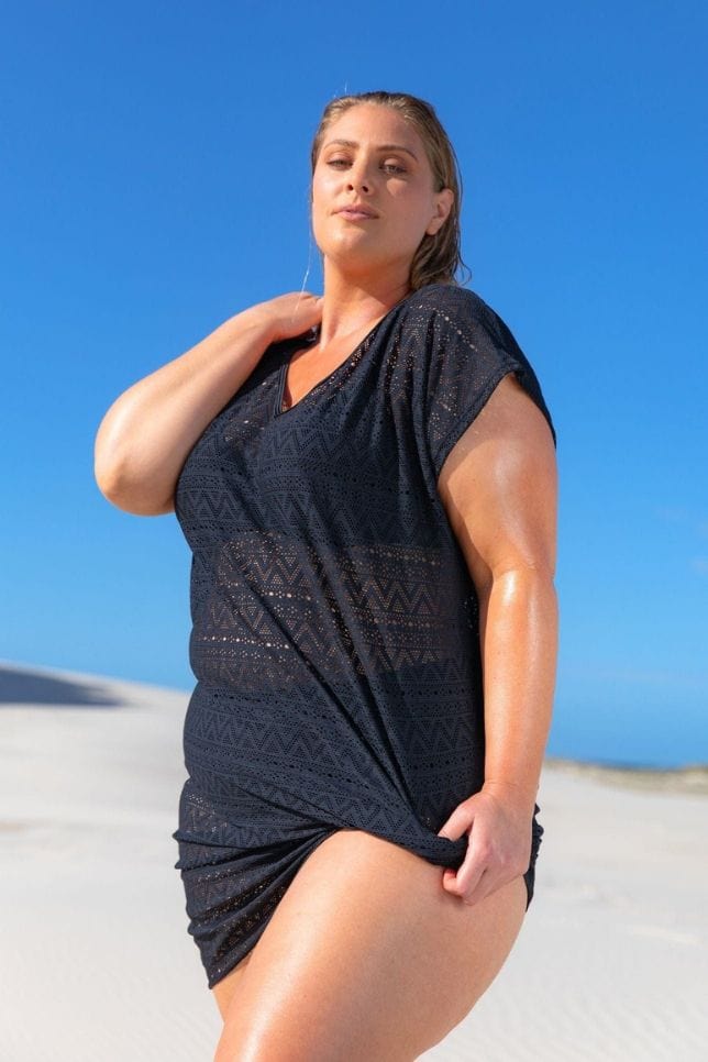 Woman stands wearing a black patterned mesh over shirt. She uses this swimsuit coverup to disguise her black bikini