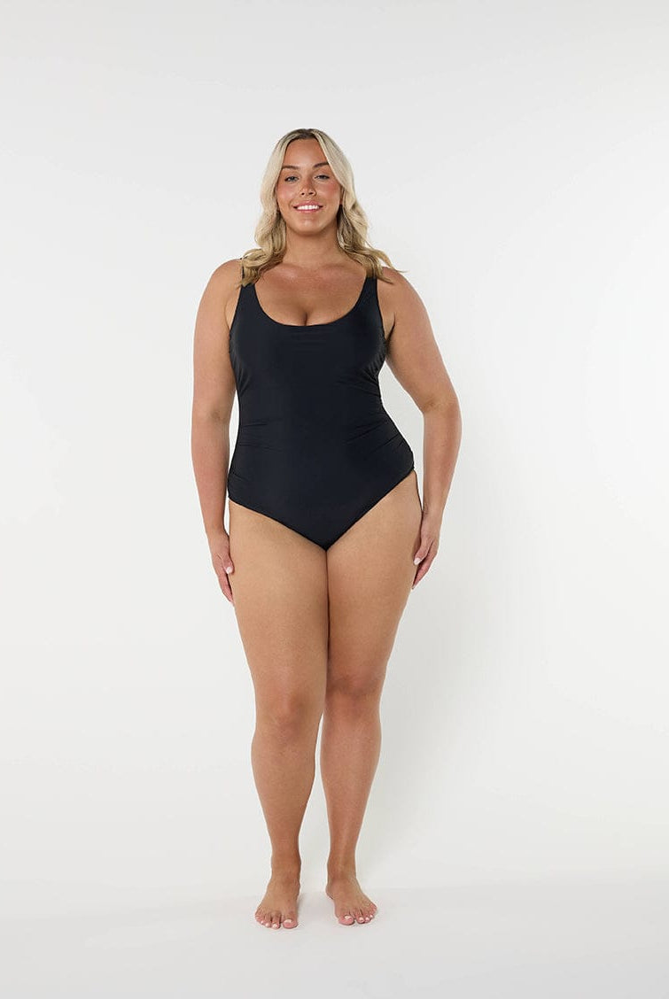 model standing in front of a white wall wearing a black one piece swimsuit