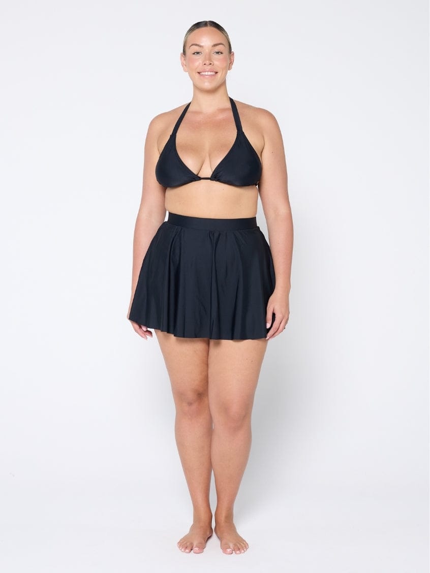 Woman wearing a black bikini set with a matching skirt on a white background