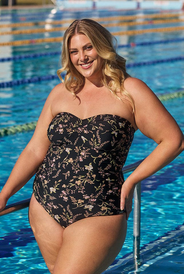 Model wearing black floral strapless one piece swimsuit at pool