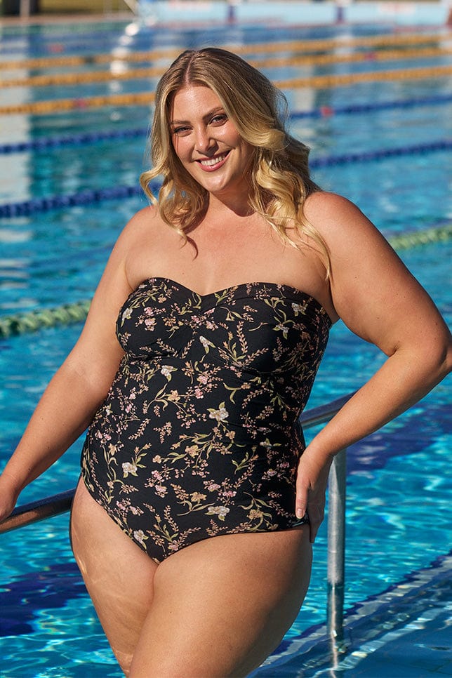 Model wearing black floral strapless one piece swimsuit at pool