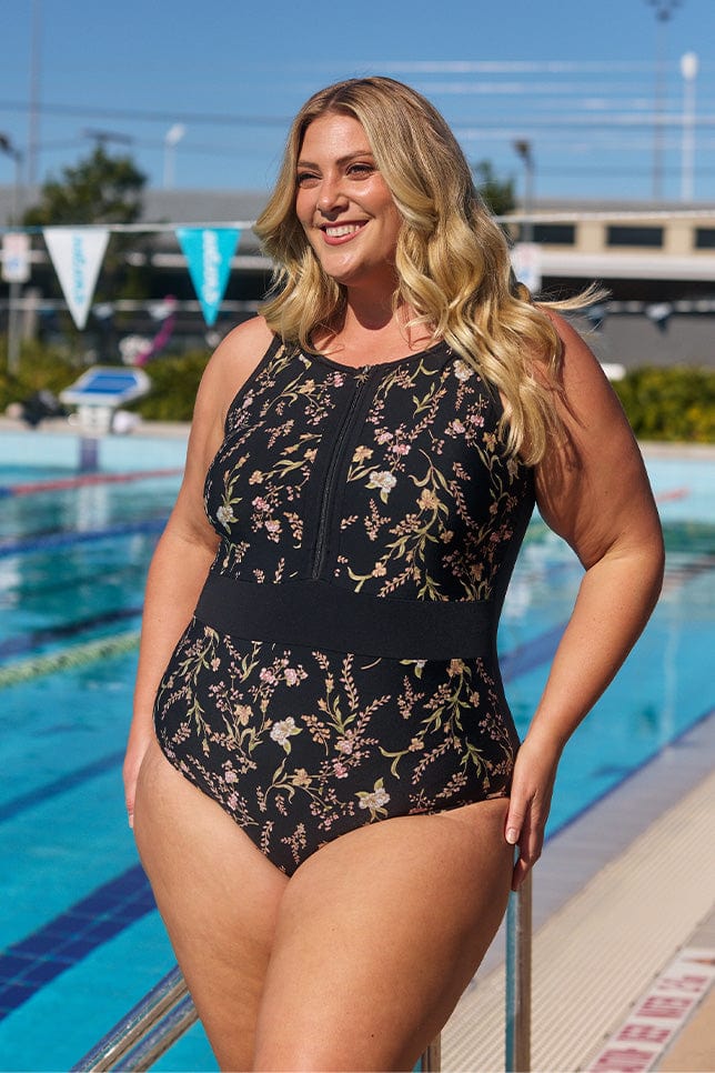 Model wearing black floral zip up one piece at pool