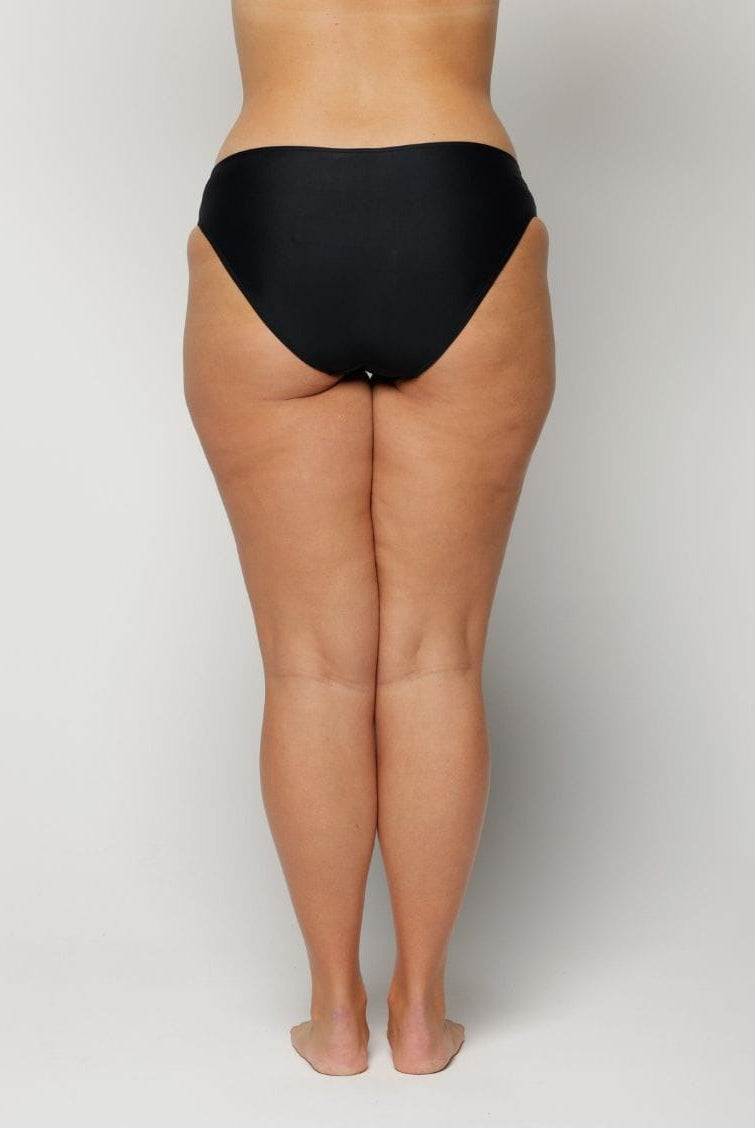 Woman wearing black underwear on a plain background