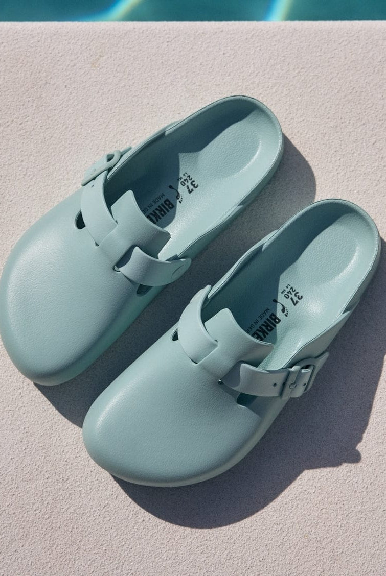 Pair of light blue clogs on a diving board with a pool in the background