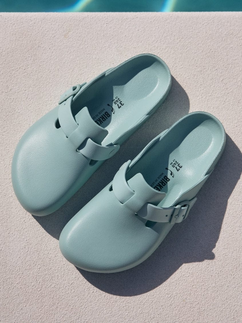 Pair of light blue clogs on a diving board with a pool in the background