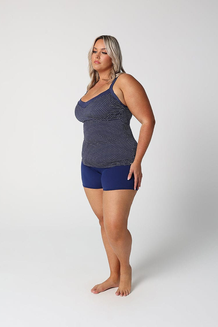 Woman wearing a navy patterned tank top and blue shorts on a white background