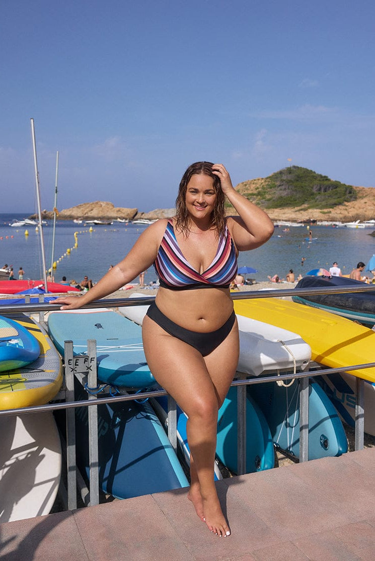 Woman in a striped bikini standing by boats on a sunny day