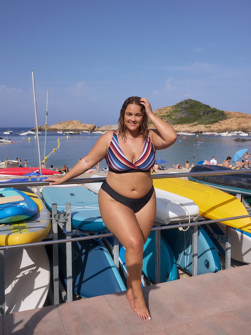 Woman in a striped bikini standing by boats on a sunny day