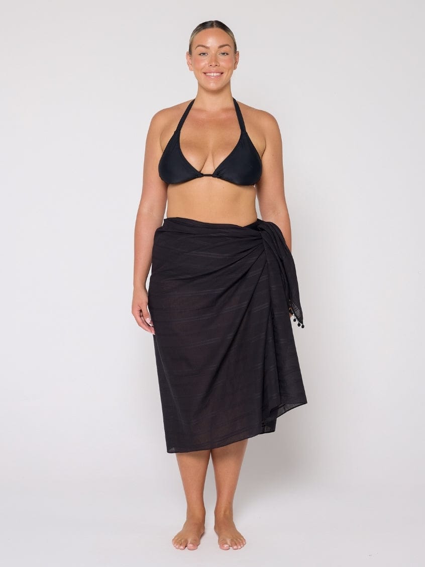 Woman wearing a black bikini and black sarong on a white background