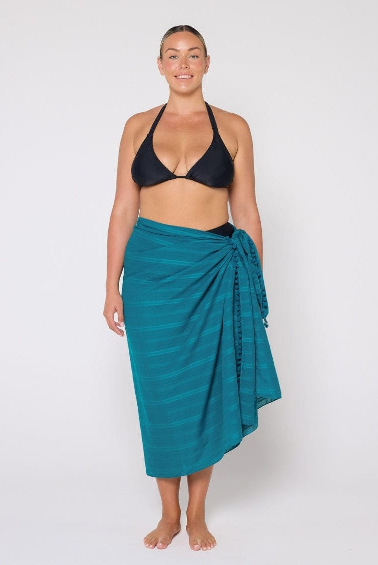 Woman wearing a black bikini top and teal sarong on a white background