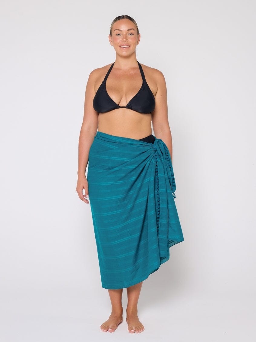 Woman wearing a black bikini top and teal sarong on a white background