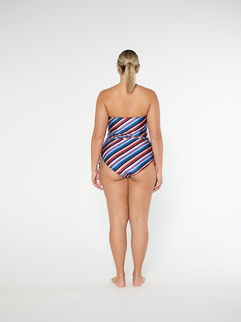 Woman wearing a strapless, multicolored striped swimsuit on a white background
