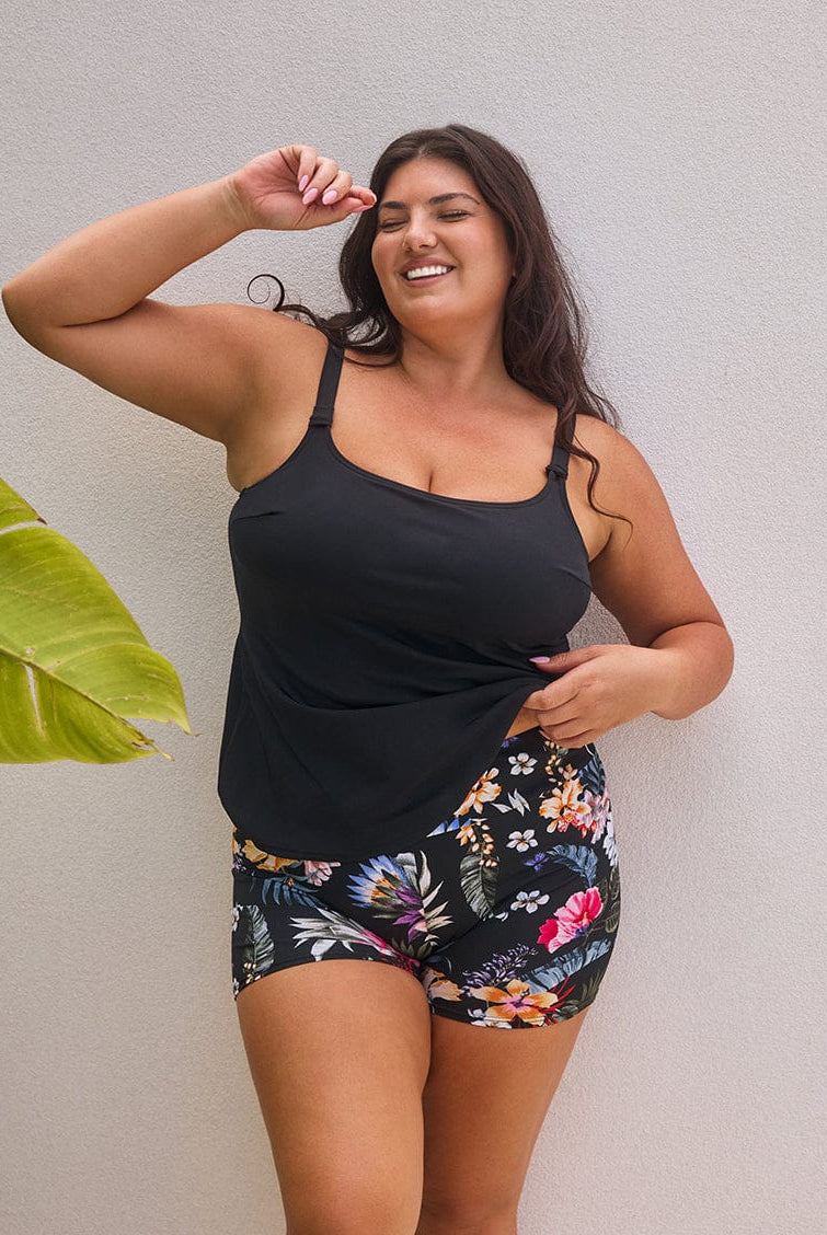 Woman wearing a black tank top and floral shorts against a plain background