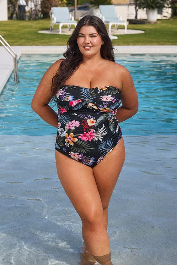Woman in a floral swimsuit standing by a pool with greenery in the background