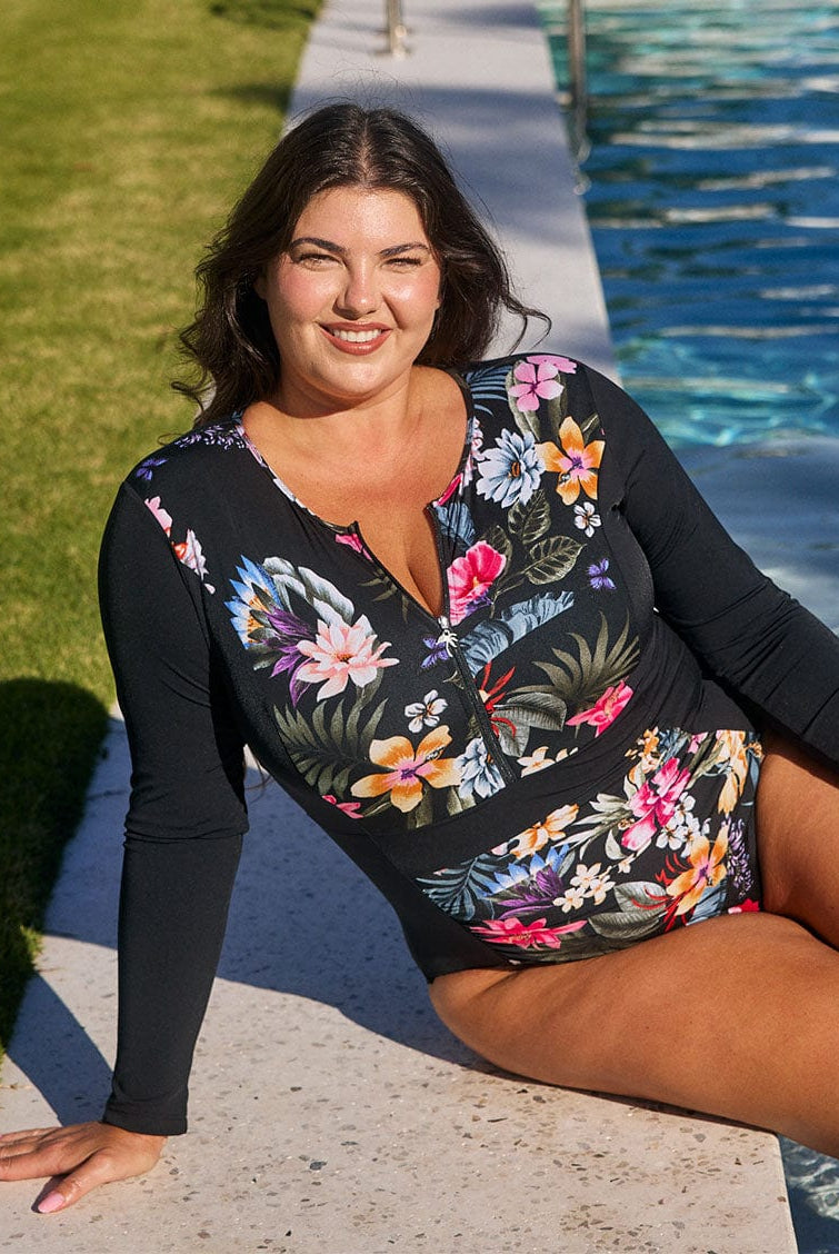 Brunette model wears flattering pool proof long sleeve one piece in black floral print