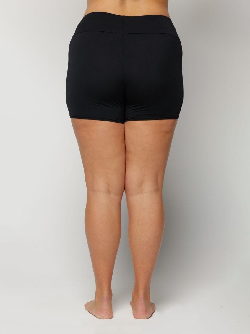 Woman wearing black swim shorts on a plain background