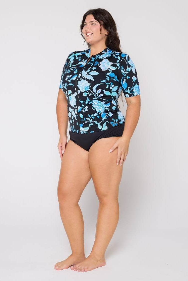 Woman wearing a black floral rash guard and black swimsuit bottoms on a white background