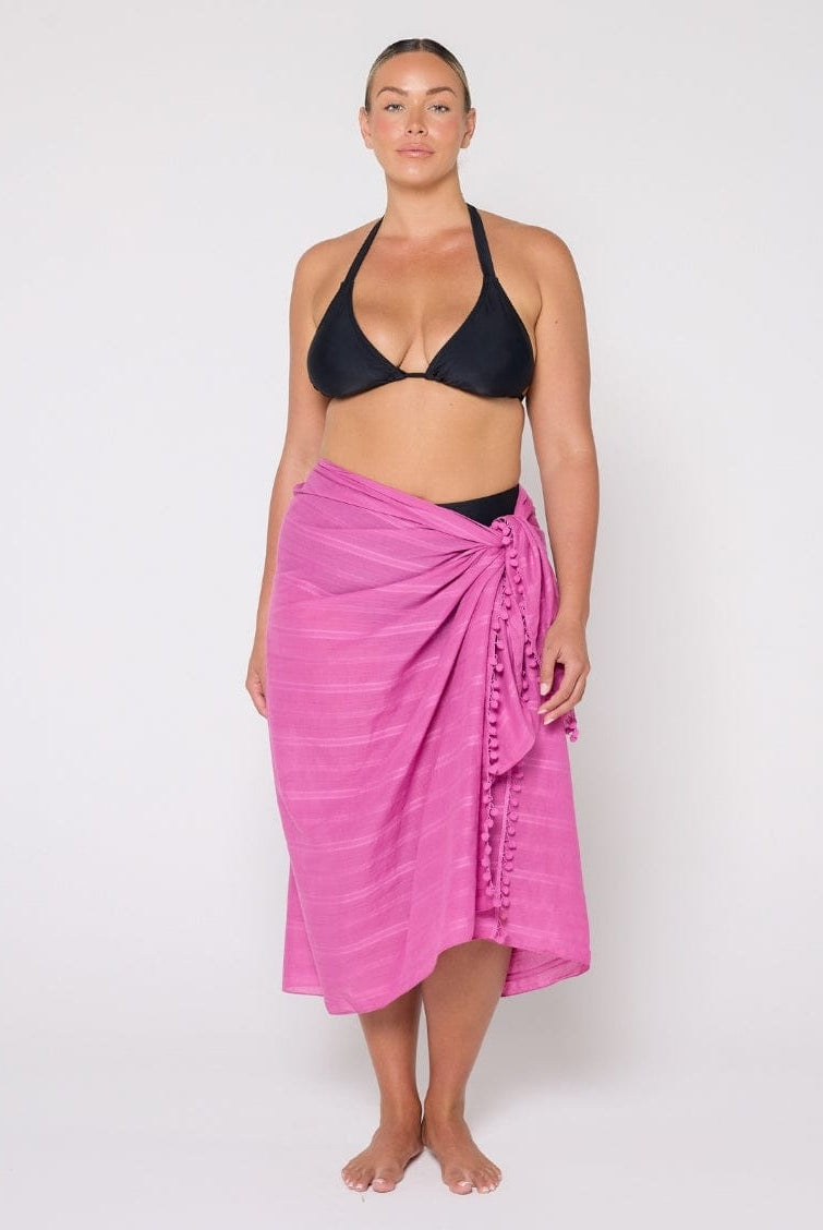 Woman wearing a black bikini and pink sarong on a white background