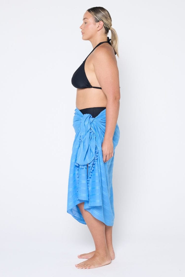 Woman wearing a black bikini top and blue sarong on a white background