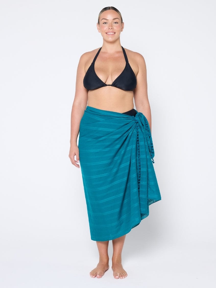 Woman wearing a black bikini top and teal sarong on a white background