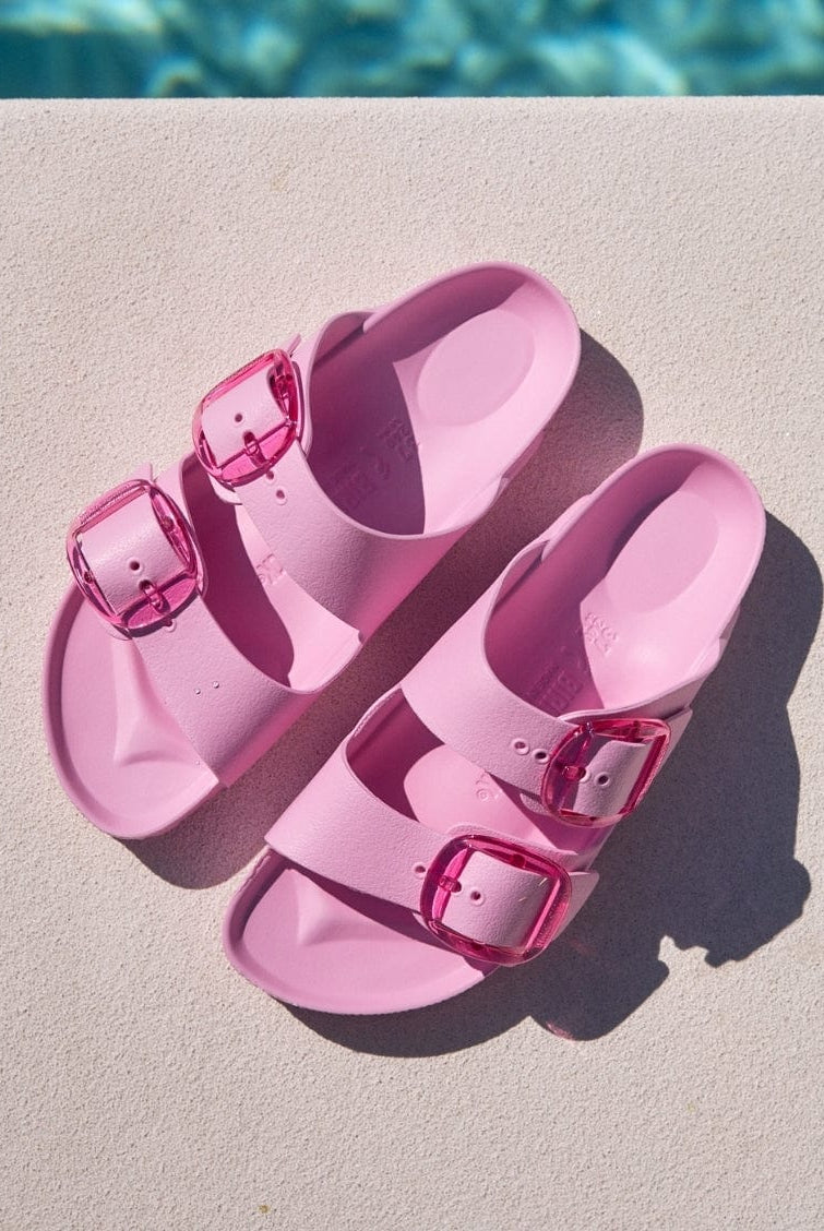 Pink sandals with buckles on a diving board near a pool.