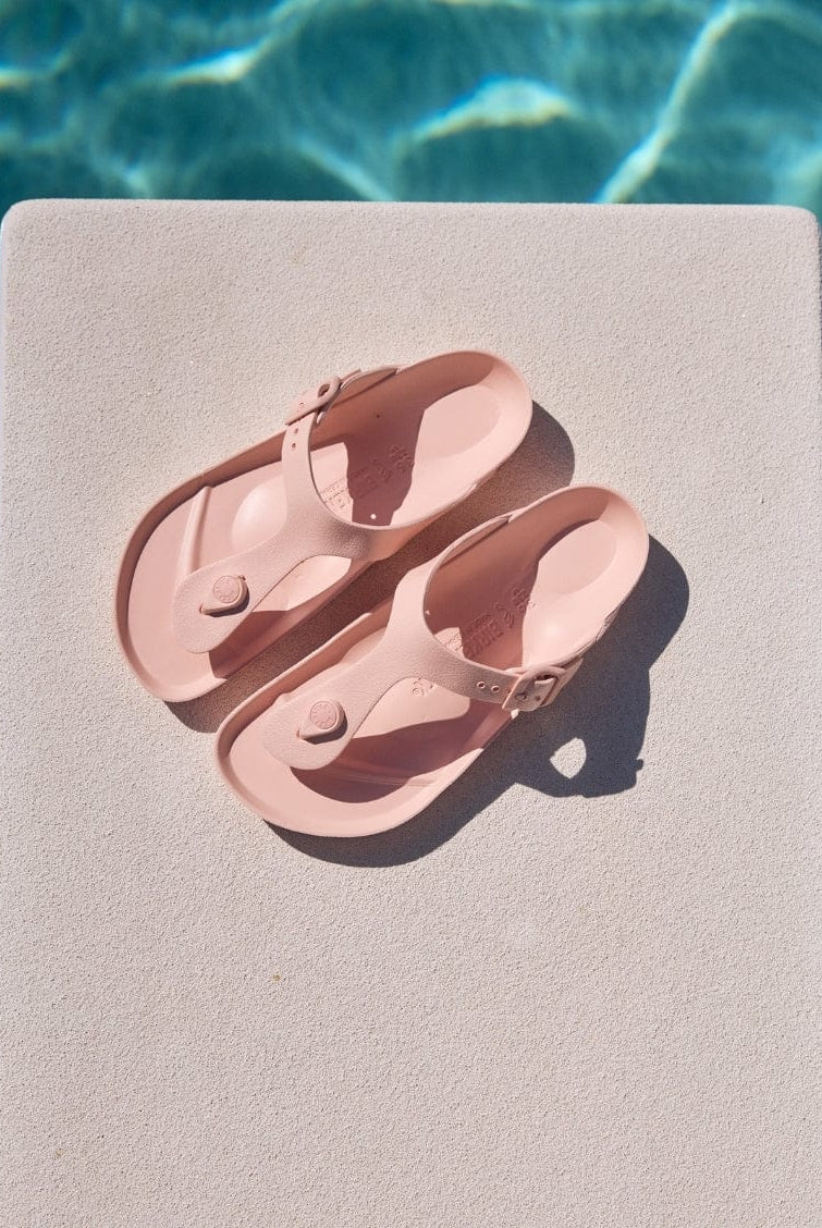 Pair of pink sandals on a diving board by a pool