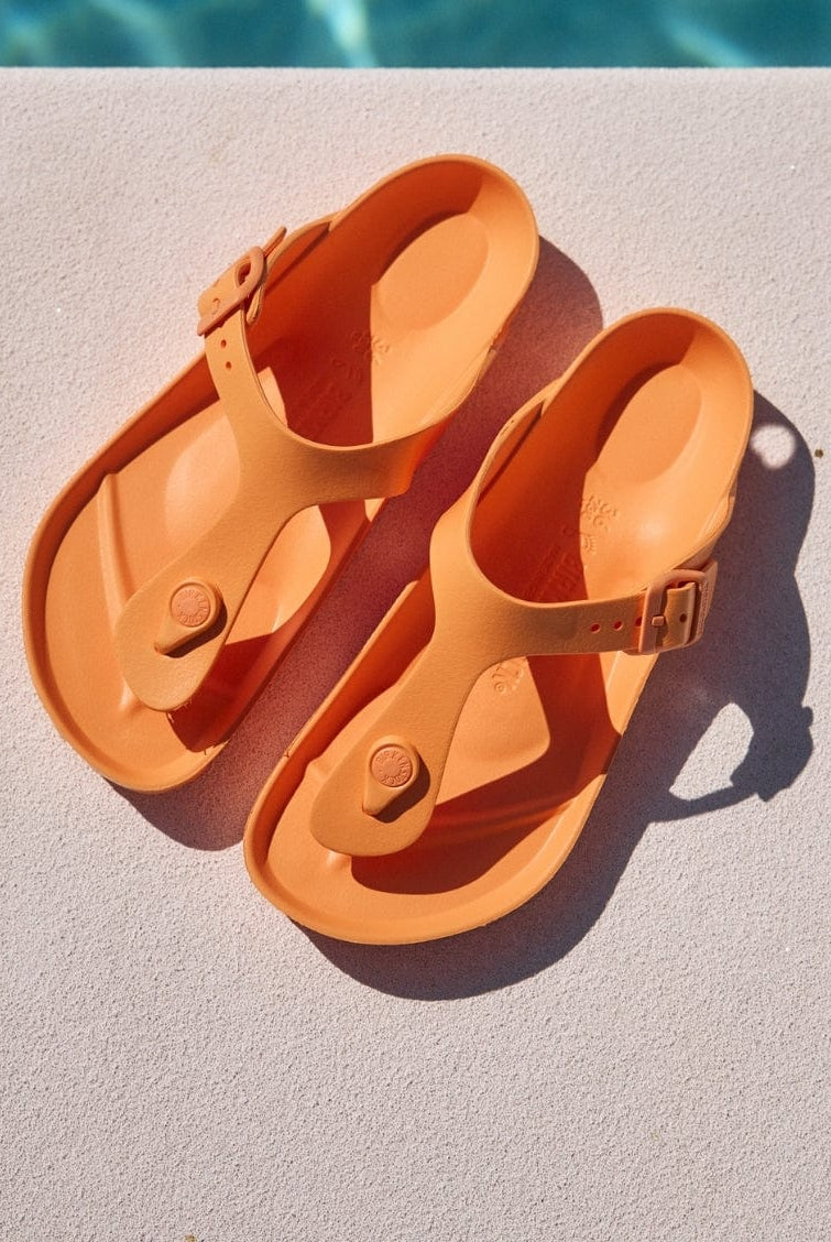Pair of orange sandals on a diving board with a pool in the background