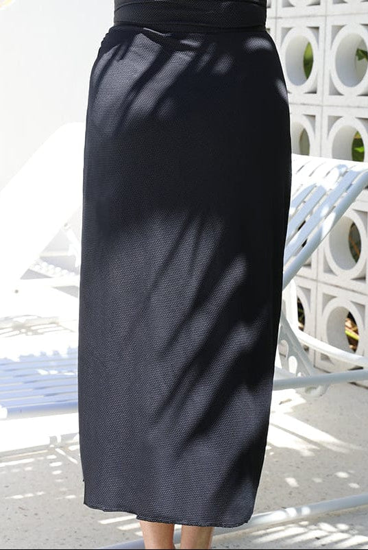 back of model standing in front of a white walling wearing a long split swim skirt in black