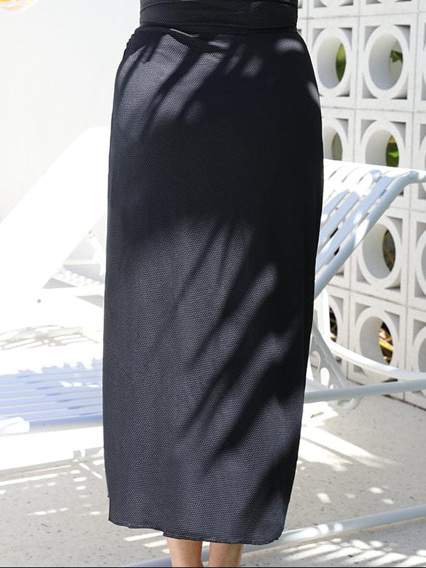 back of model standing in front of a white walling wearing a long split swim skirt in black
